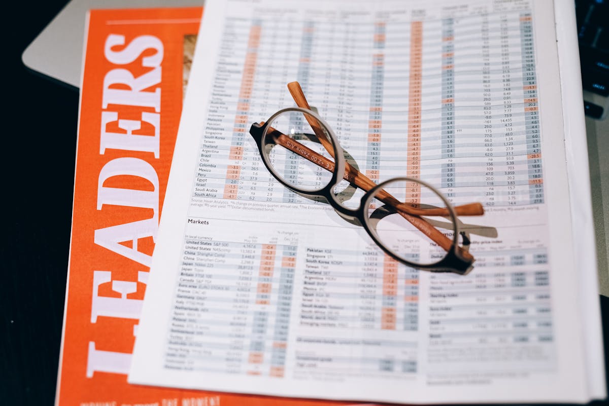 A pair of eyeglasses resting on a financial document and magazine with bold headline