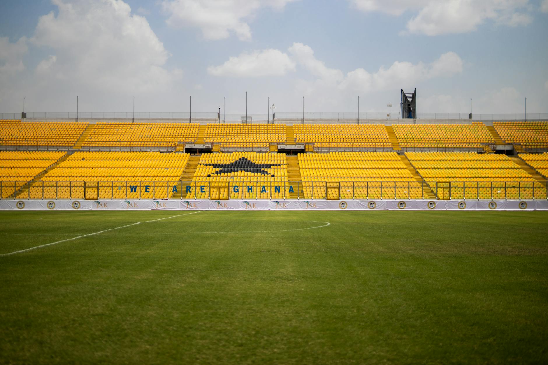 Stadium with bright yellow seats and green lawn under a blue sky in Ghana. Ideal for sports events.